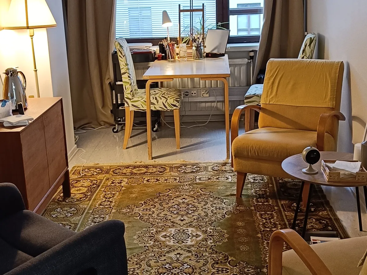 Vastaanottohuone Helsingissä: keltaiset nojatuolit, työpöytä ikkunan edessä, lipasto ja vihreä itämainen matto.